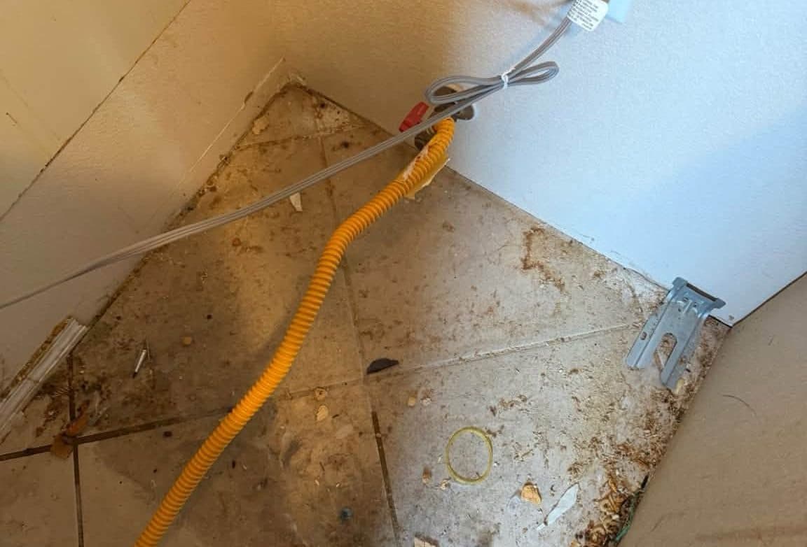 Laundry hookup corner with a dirty tile floor before a move-out cleaning