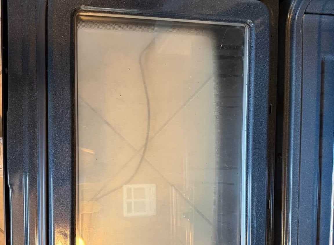 Oven door glass and interior coated in baked-on grease before an oven deep cleaning