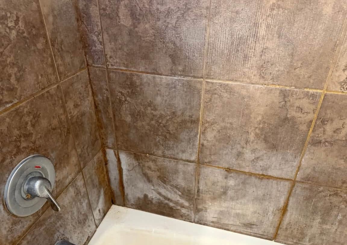 Shower wall tile with hard water scale around the valve before a deep cleaning